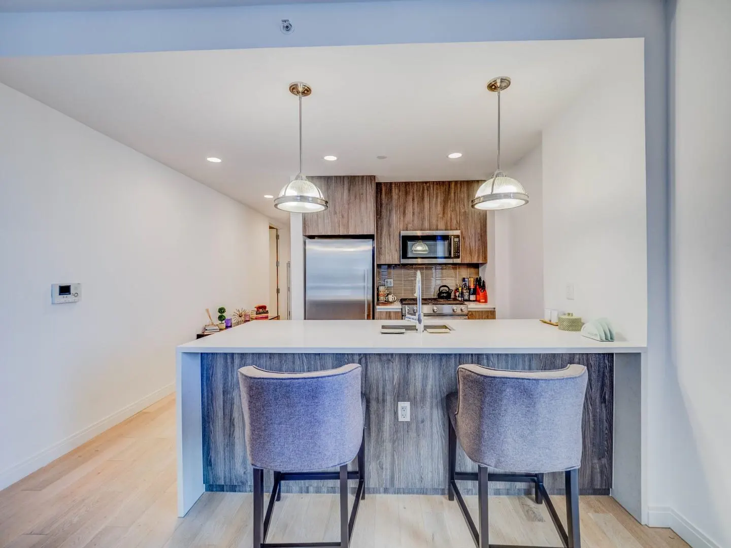 A modern kitchen with a white countertop island, two blue chairs, and stainless steel appliances.
