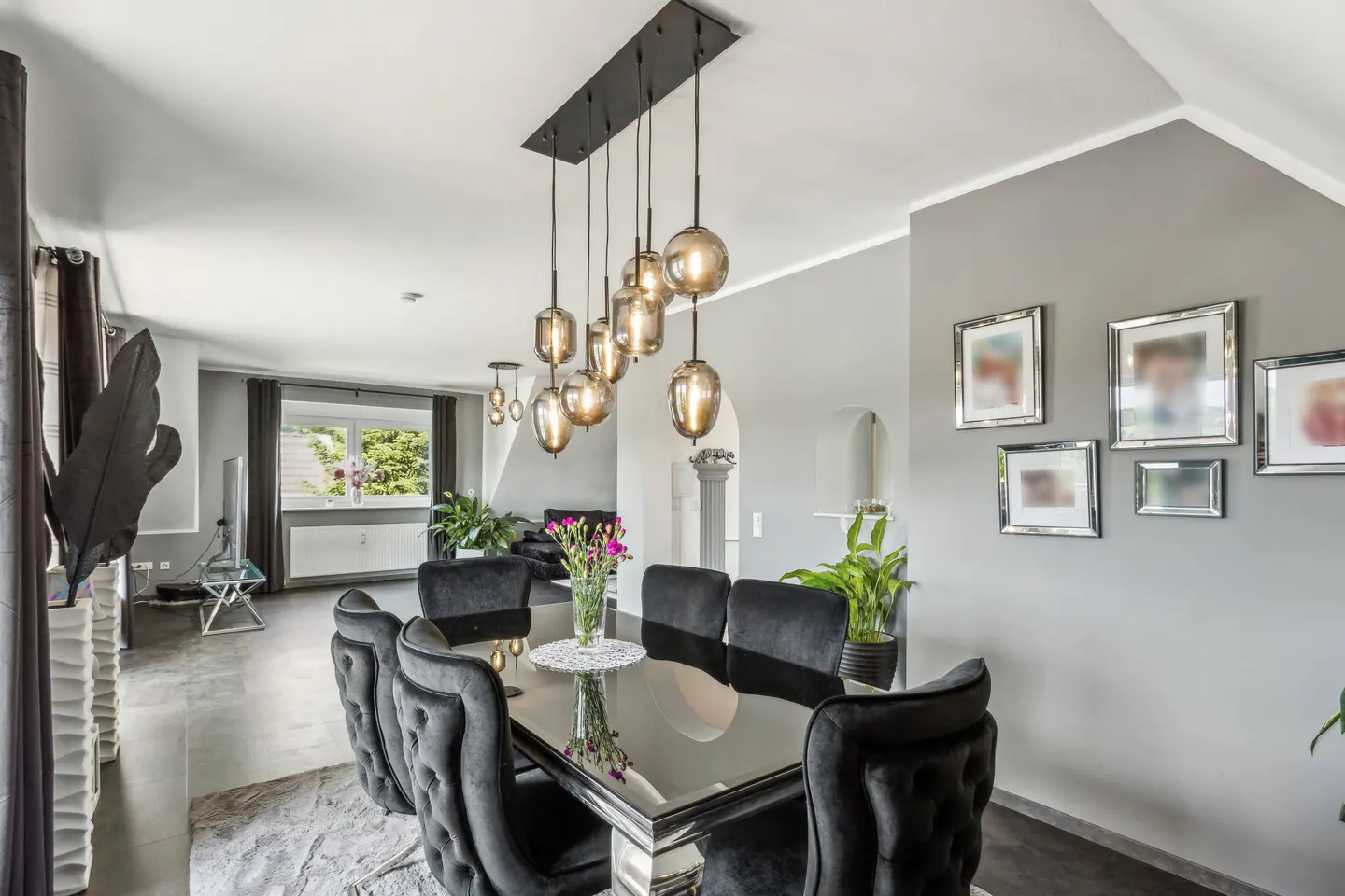 Modern dining room with a black glass table, tufted black chairs, and a cluster of hanging glass pendant lights.