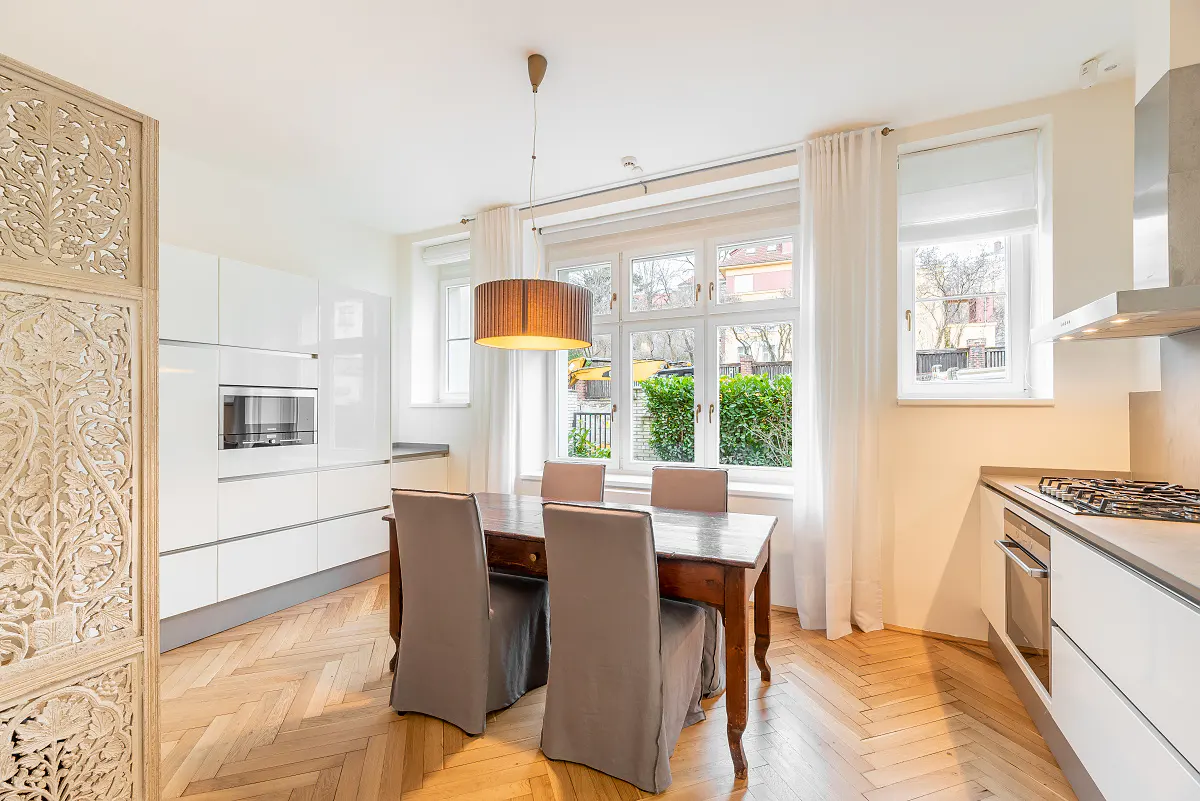 Modern kitchen with white cabinets, wooden herringbone floors, and a dining table with grey chairs under a pendant light.