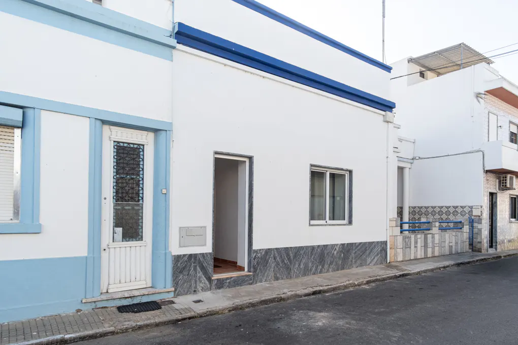 Exterior of a white building with blue trim, featuring a door with a decorative window and an open doorway.