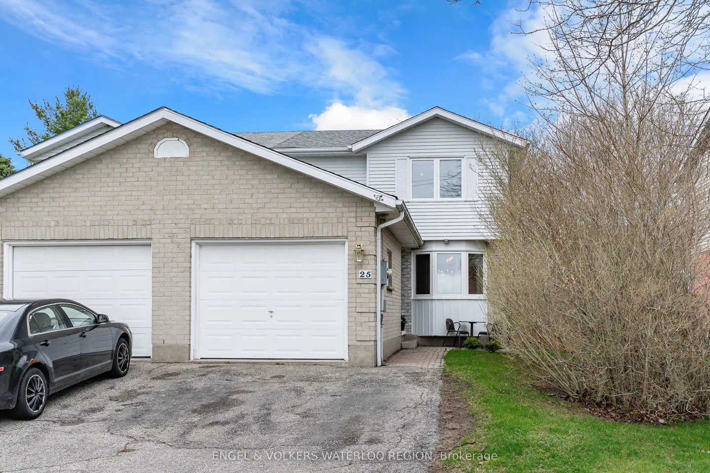 Two-story townhouse with a brick and light gray exterior, two white garage doors, and a black car parked in the driveway.