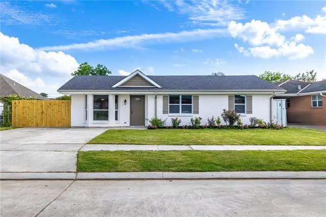 A white, single-story house with a gray roof, brown door, and green lawn under a blue sky.