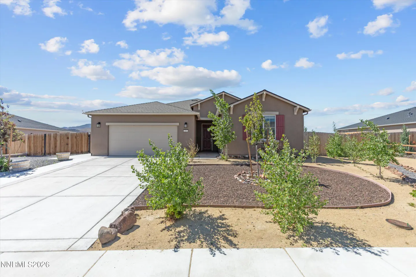 Tan single-story house with a gray roof, a two-car garage, and a concrete driveway under a blue sky with white clouds.