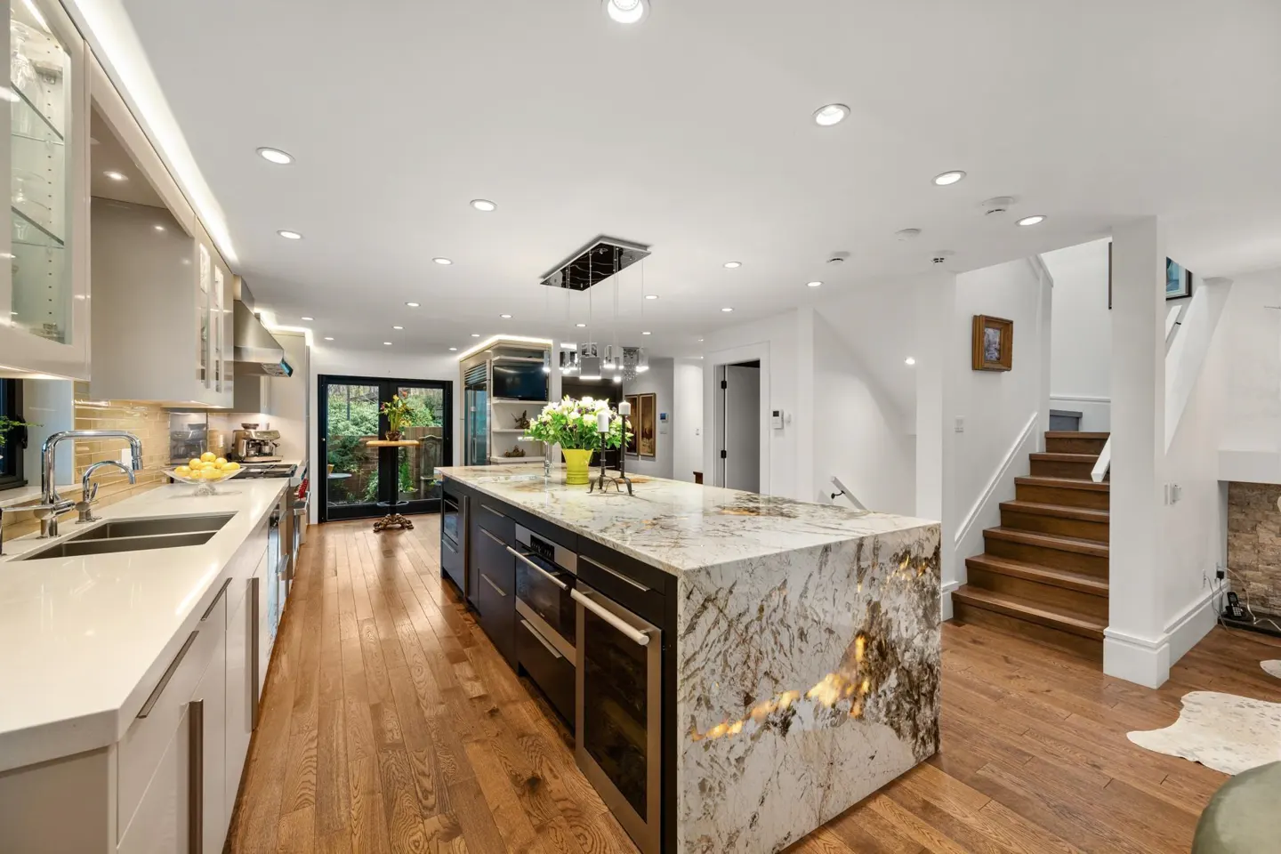 Bright, modern kitchen with white cabinets, marble island, and hardwood floors. Stairs lead to the upper level.