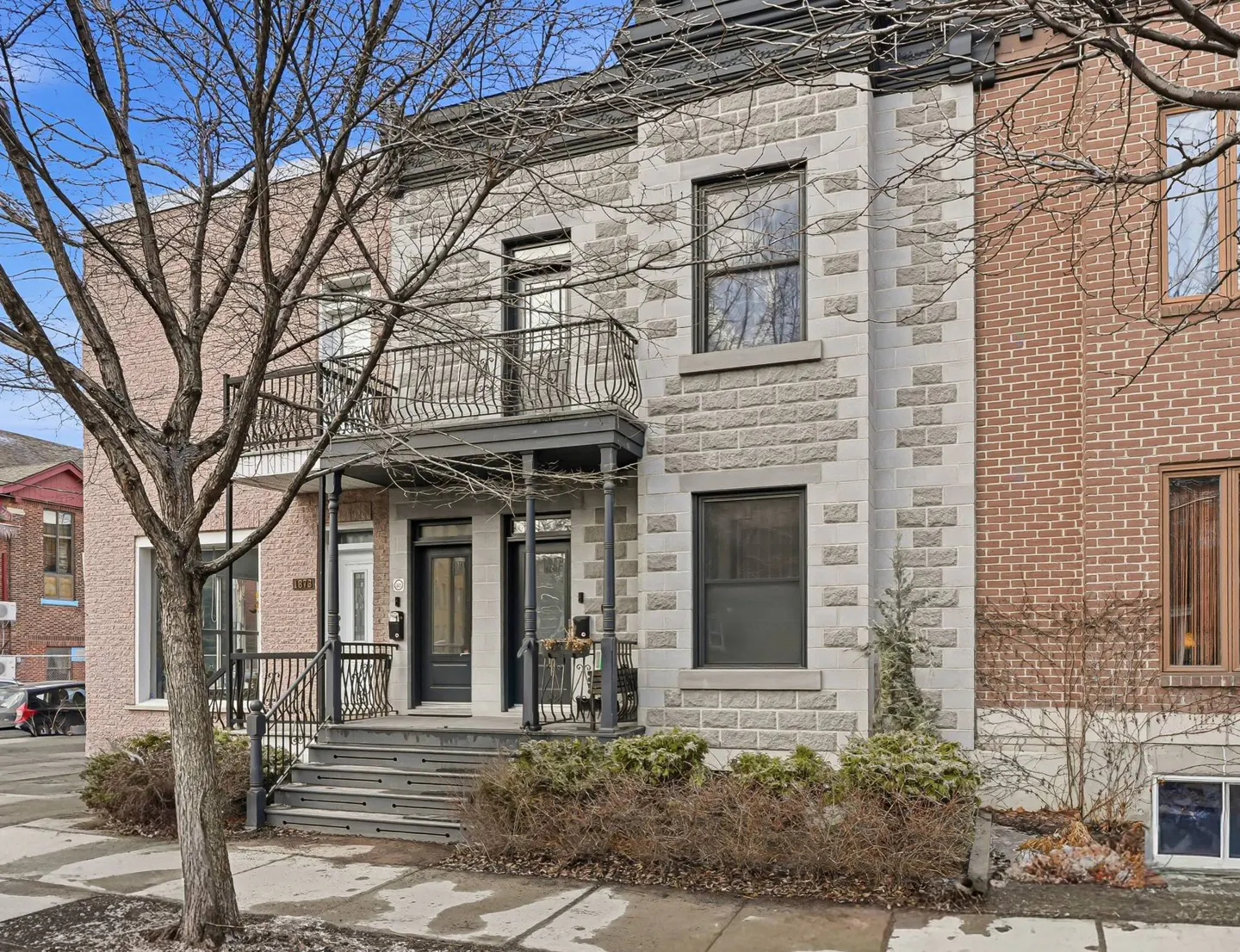 Exterior view of a two-story row house with stone and brick facade, black doors, and wrought iron balconies.