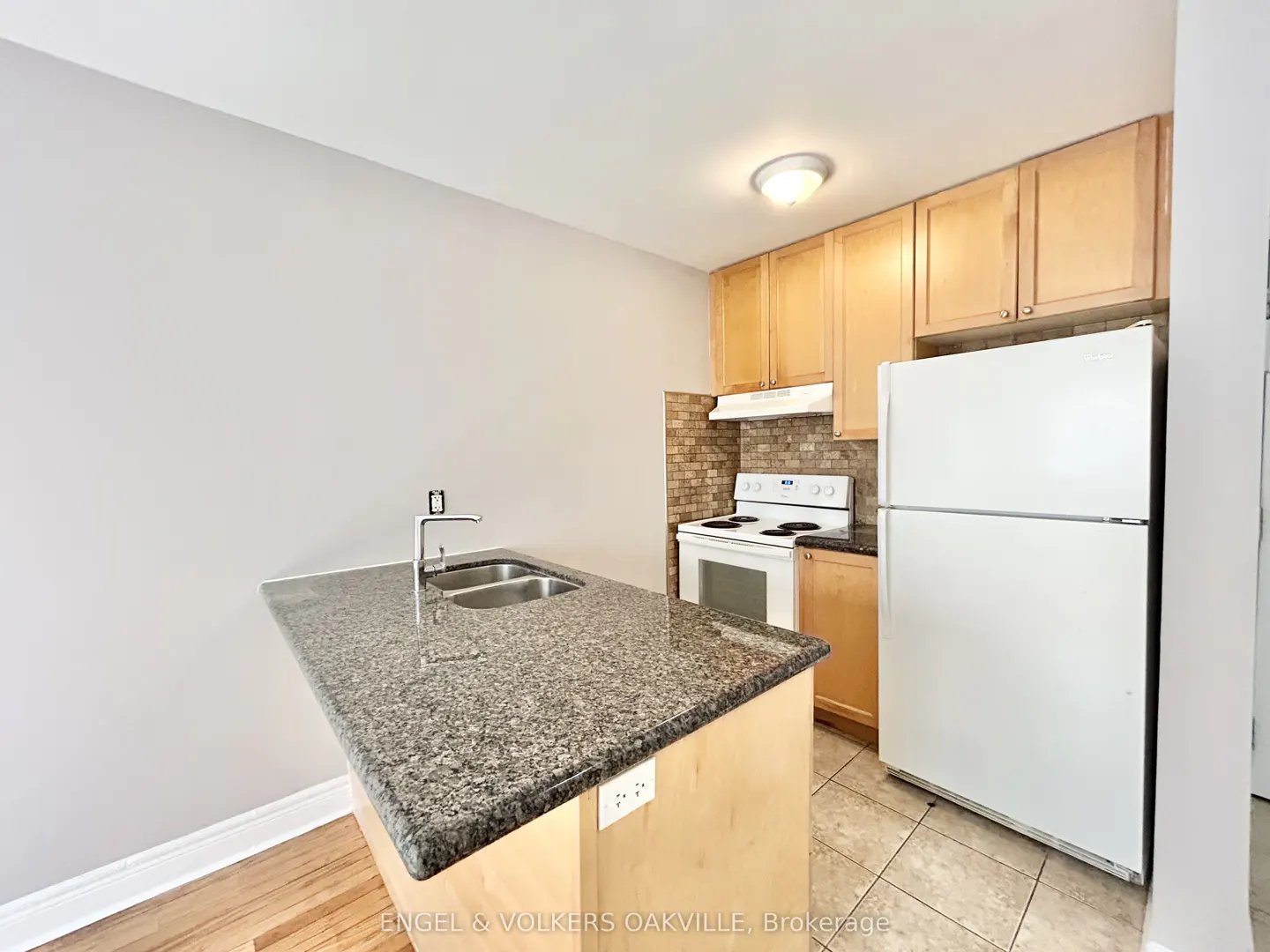 A kitchen with light wood cabinets, a white refrigerator and stove, and a granite countertop island with a stainless steel sink.
