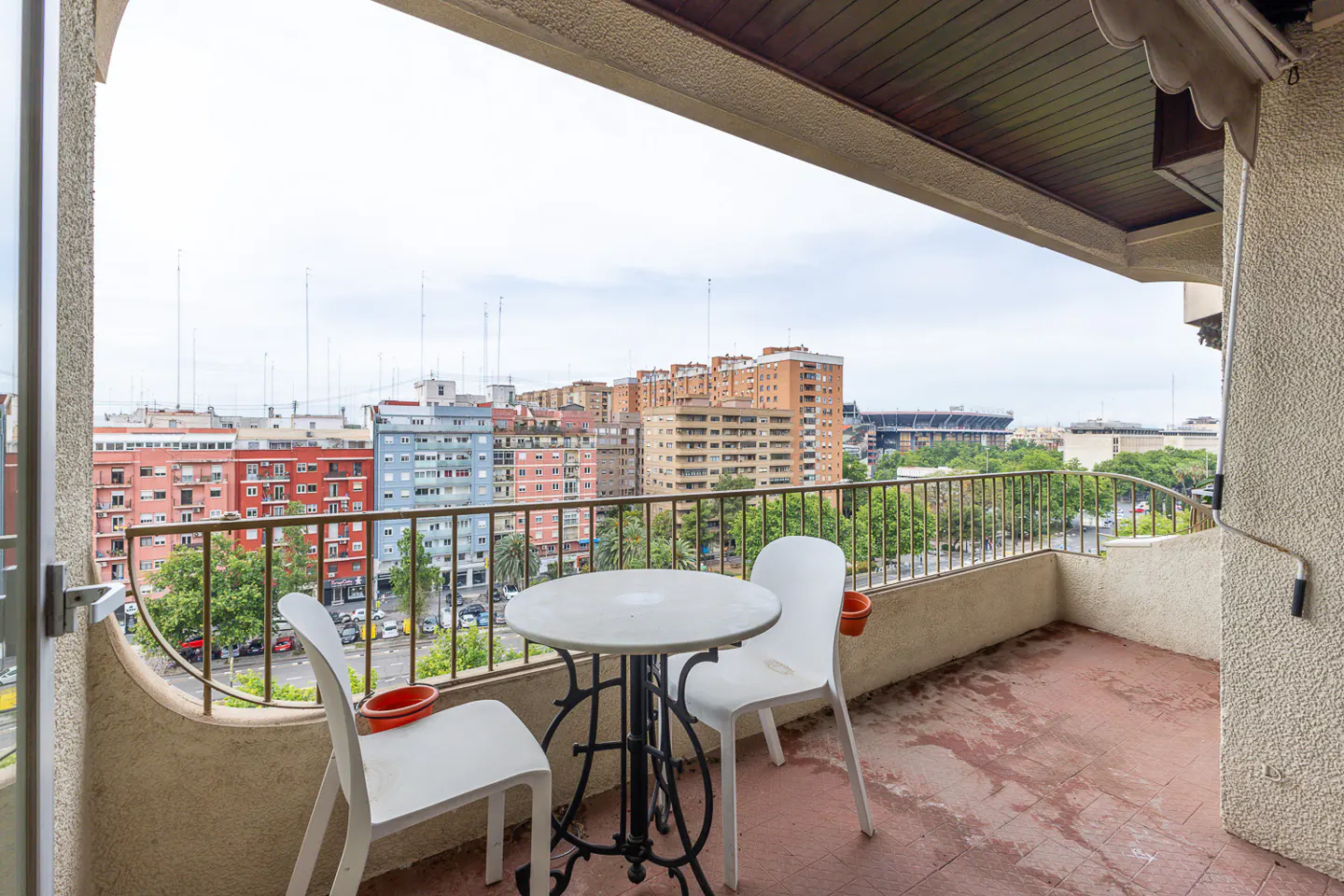 Balcony view with a round table and two white chairs overlooking a cityscape with colorful buildings and a stadium.