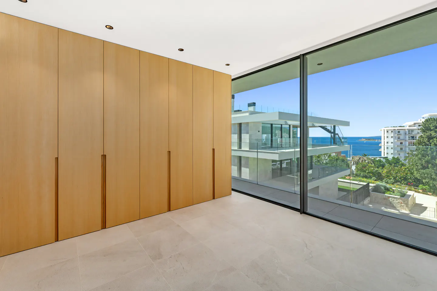 A bright room with a large window showing a coastal view. A light wood closet stands against one wall.