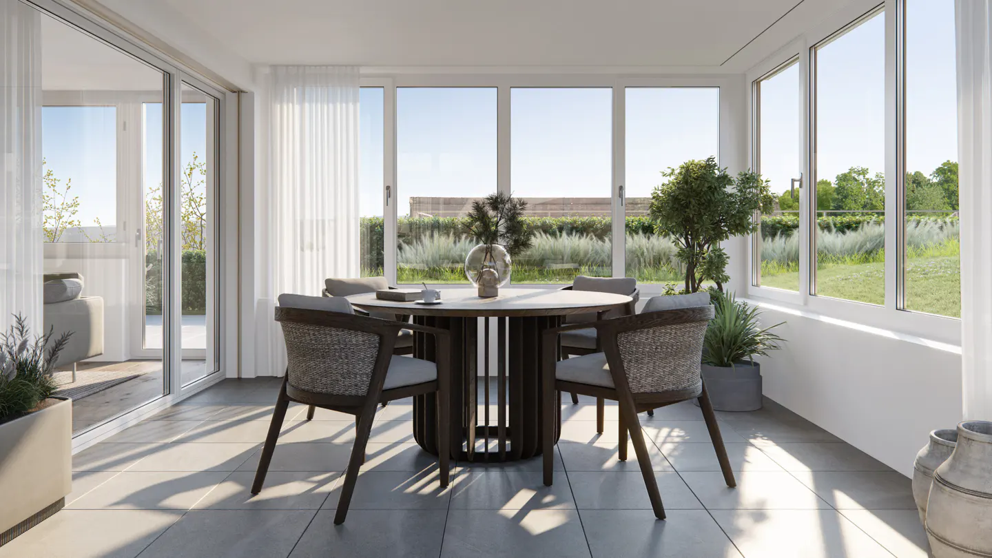 Bright sunroom with a round table, four chairs, and large windows overlooking a green landscape.