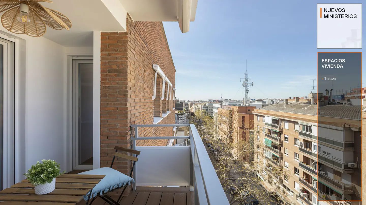 Balcony view with a small table, chair, and plant. Brick building and city skyline in the background under a blue sky.