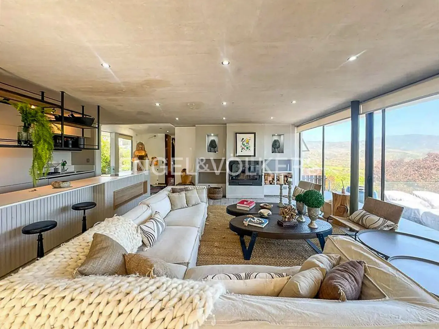 Open-concept living room with a white sectional sofa, fireplace, and floor-to-ceiling windows with a view of the landscape.