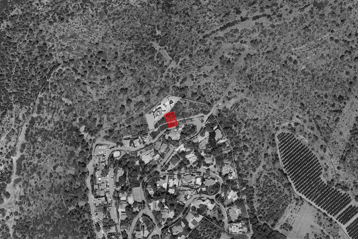 Aerial view of a property outlined in red, nestled in a neighborhood near a wooded area.