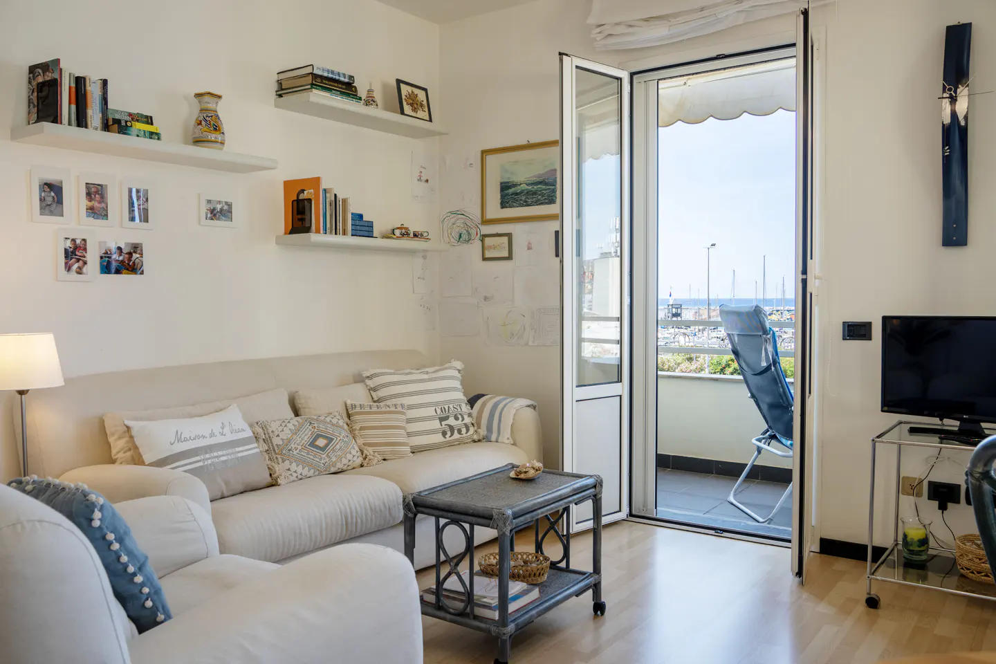 Cozy living room with a white sofa, patterned pillows, a small coffee table, and a balcony door overlooking a marina.