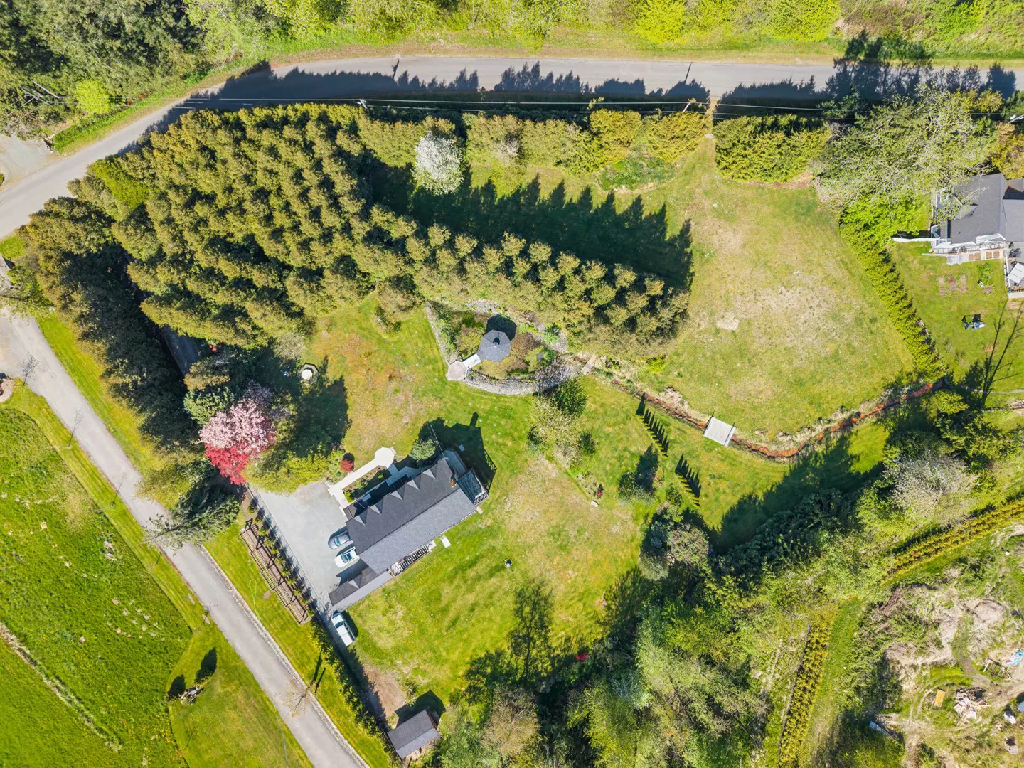 Aerial view of a property with a house, green lawn, trees, and a small gazebo in a garden area.