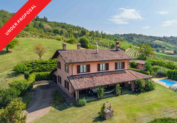 Two-story peach-colored villa with a tiled roof, porch, and pool, set in a scenic landscape with rolling green hills. [AI-generated text]
