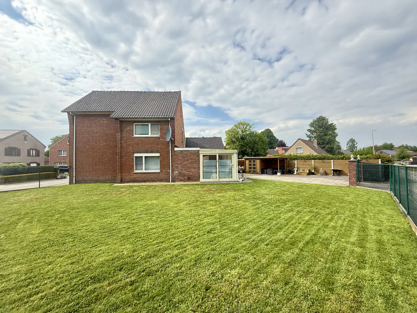 Two-story red brick house with a large green lawn under a cloudy sky.