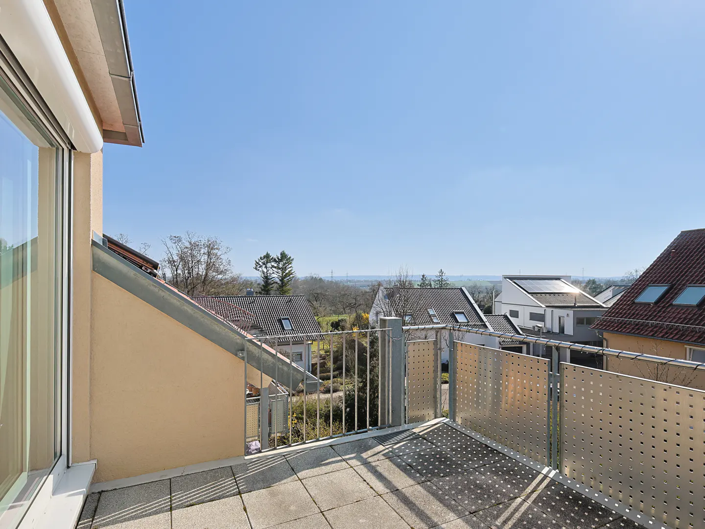 Balcony view with metal railings overlooking houses and trees under a clear blue sky.