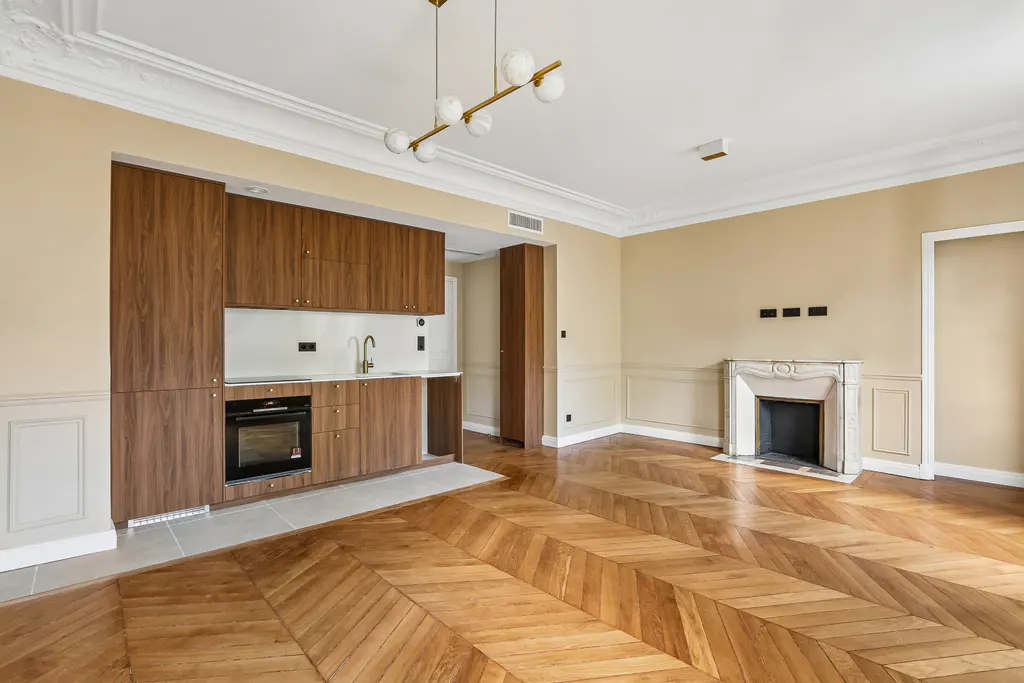 Modern kitchen with wood cabinets, chevron hardwood floors, and a fireplace in a beige room with a globe chandelier.
