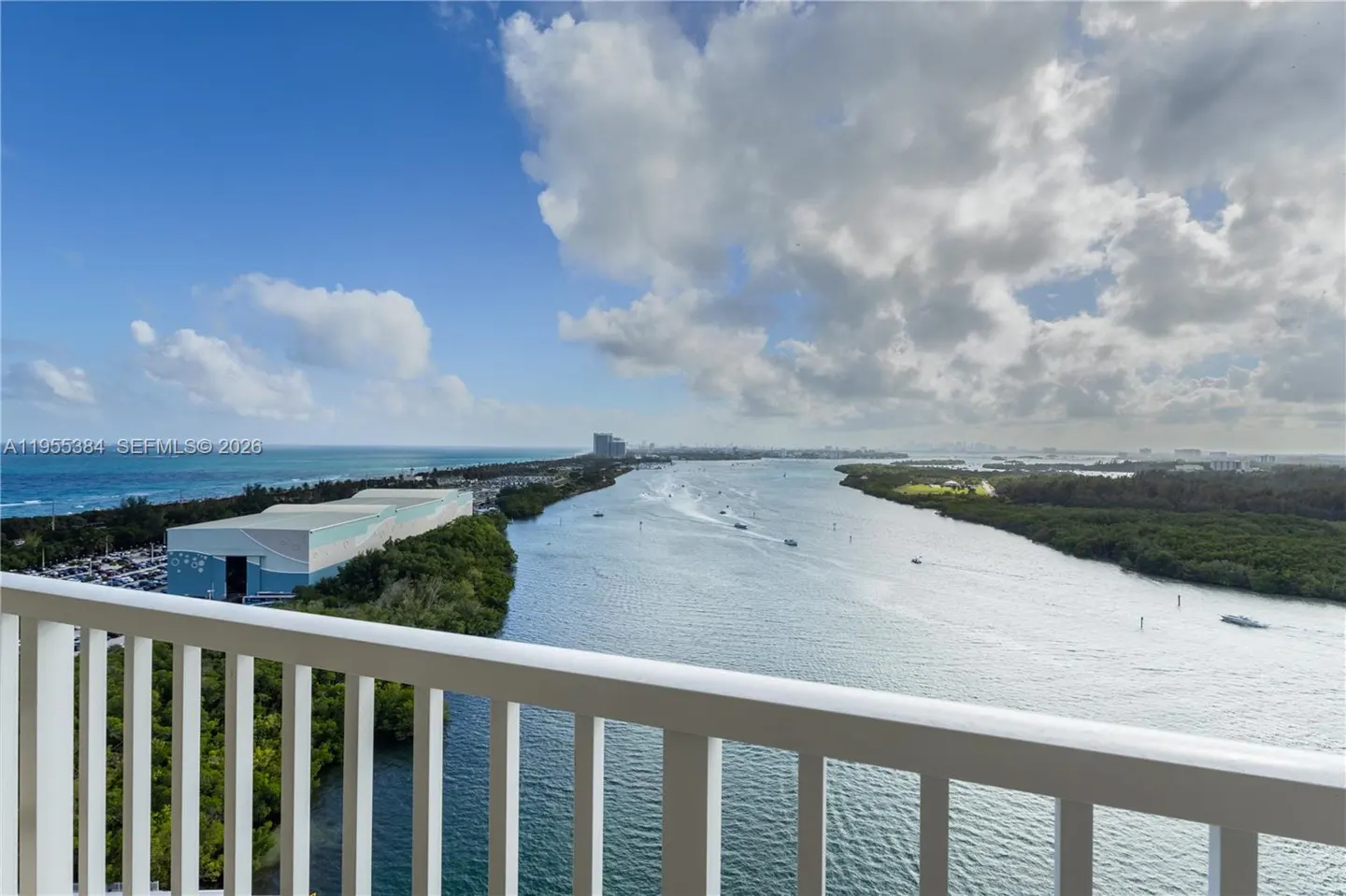 Balcony view of a waterway with boats, green islands, and the ocean under a cloudy blue sky. White railings are in the foreground.