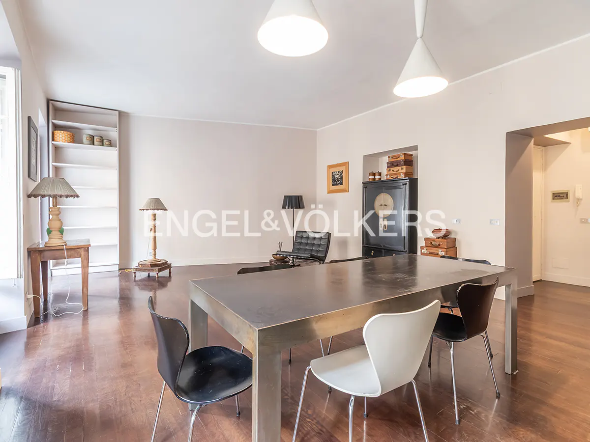 Modern dining room with a large metal table, black and white chairs, hardwood floors, and minimalist decor.