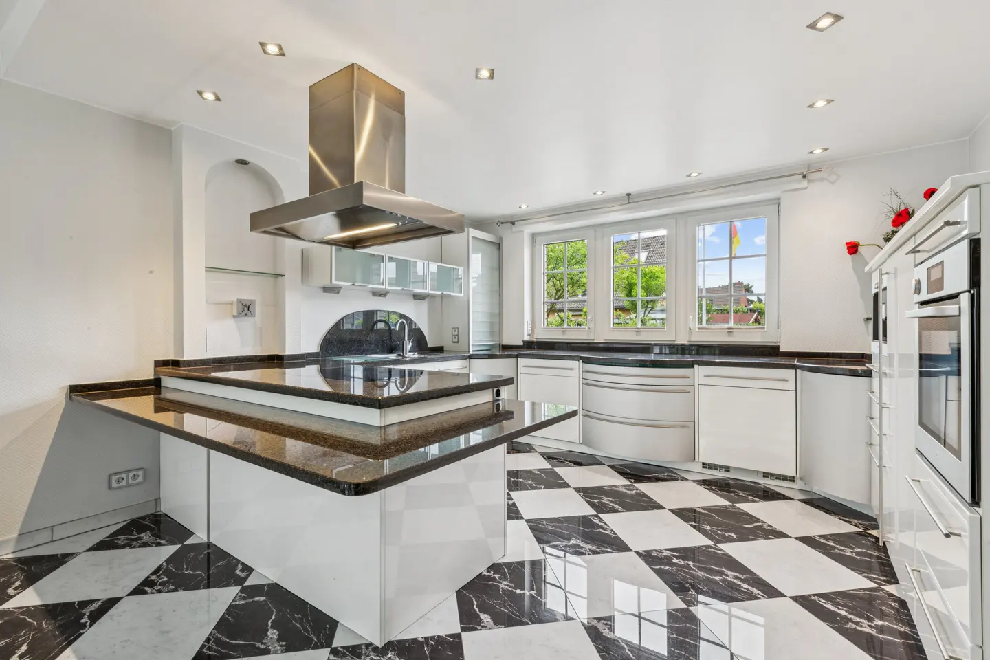 A modern kitchen with black and white checkered floors, white cabinets, and a black countertop island.