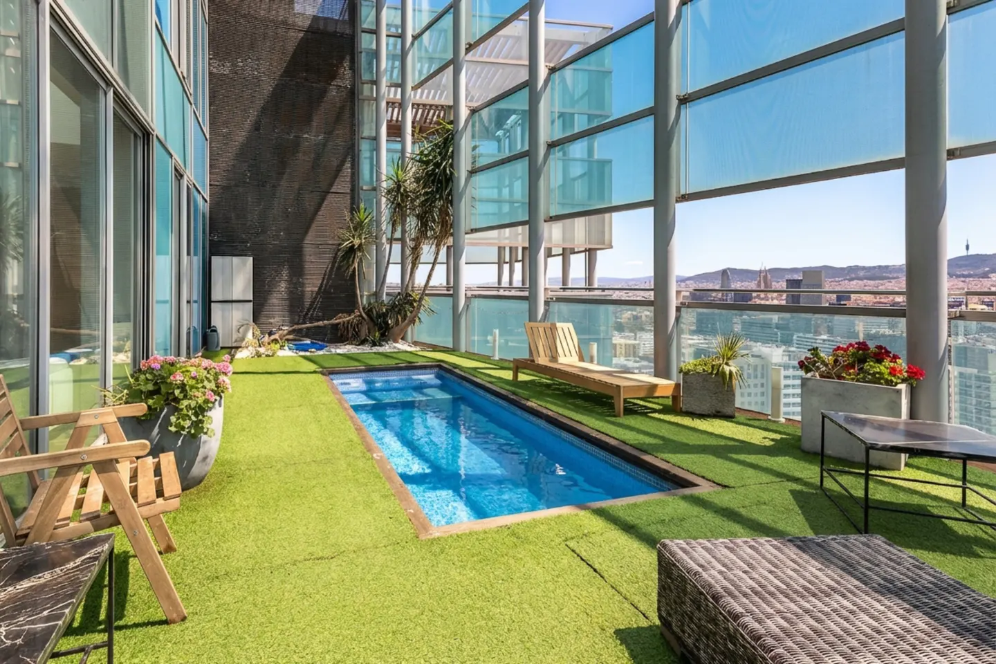Rooftop terrace with a small pool, lounge chair, and city view. Green artificial grass covers the floor.