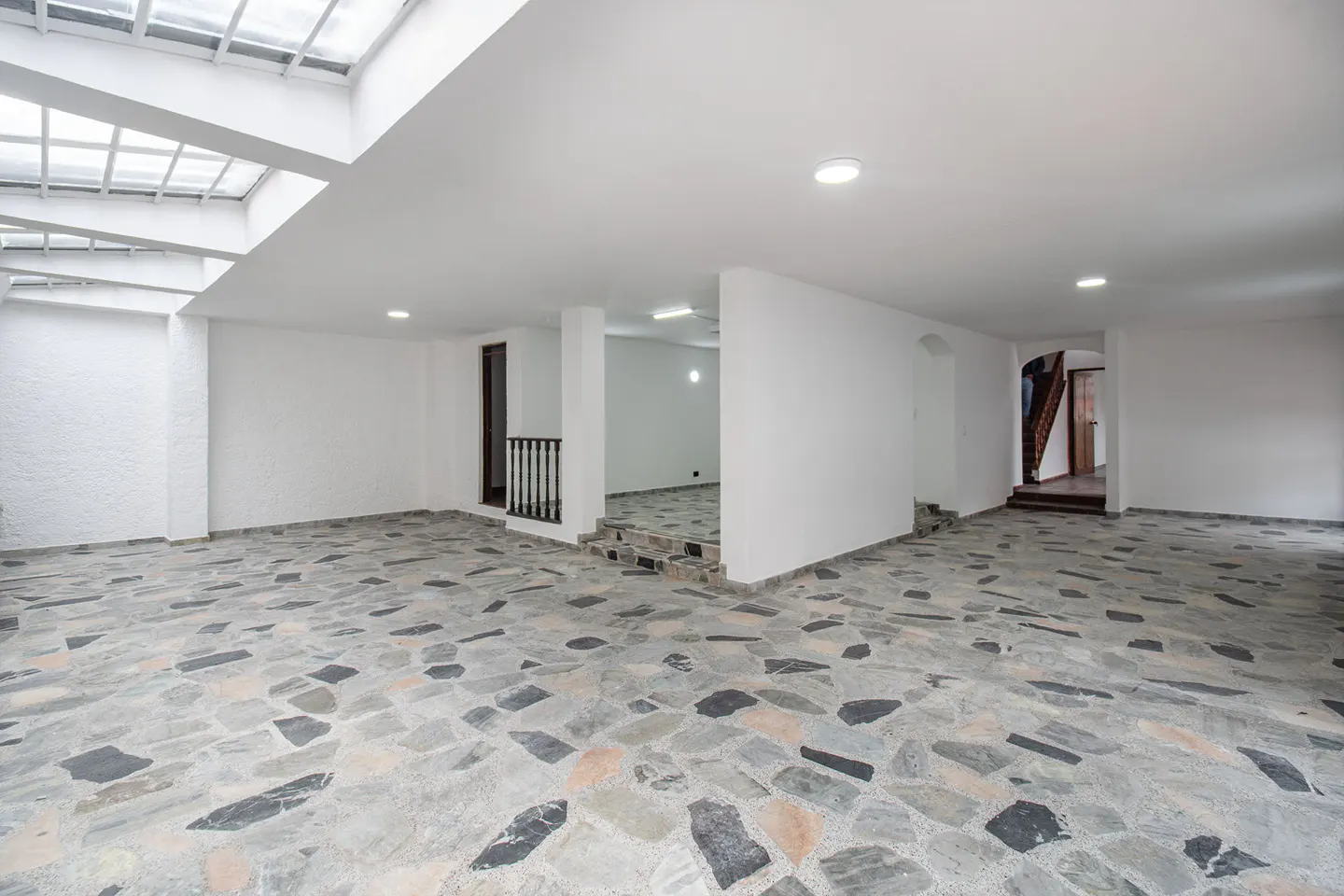 Empty room with white walls, stone tile floor, and skylight. Stairs lead to another room.