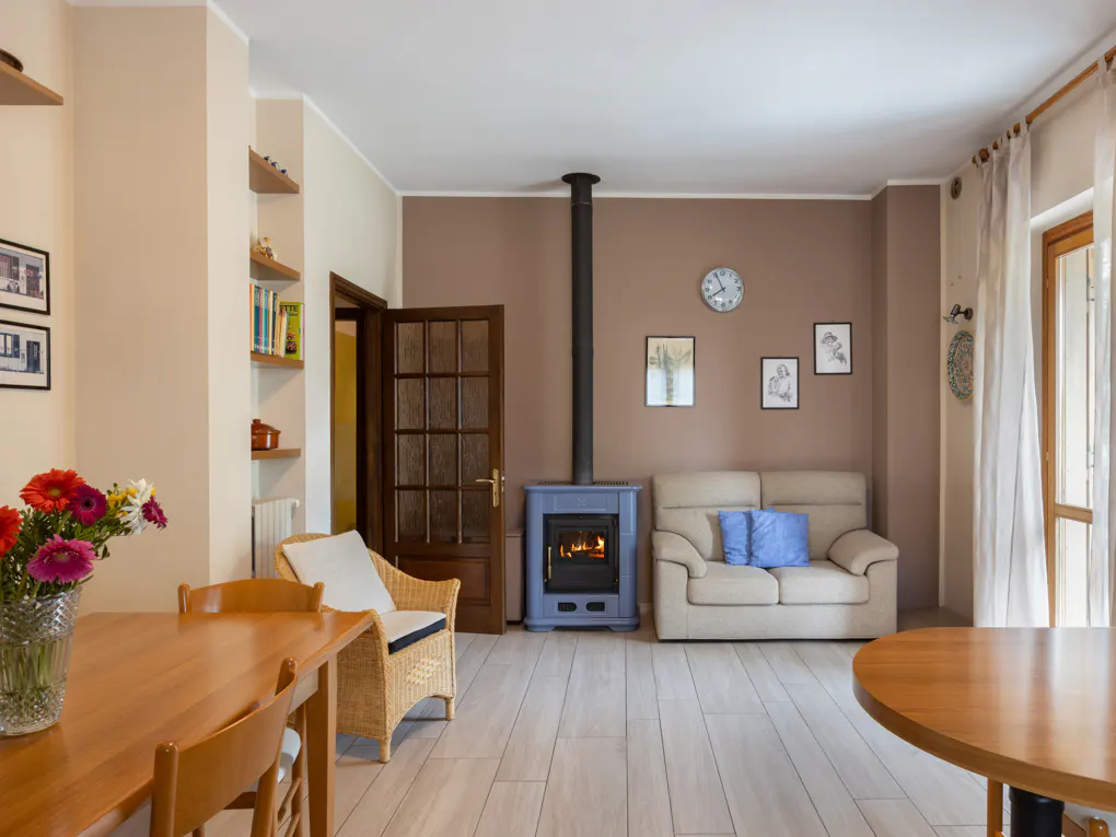 Cozy living room with a blue fireplace, beige sofa with blue pillows, and wooden dining table with flowers.