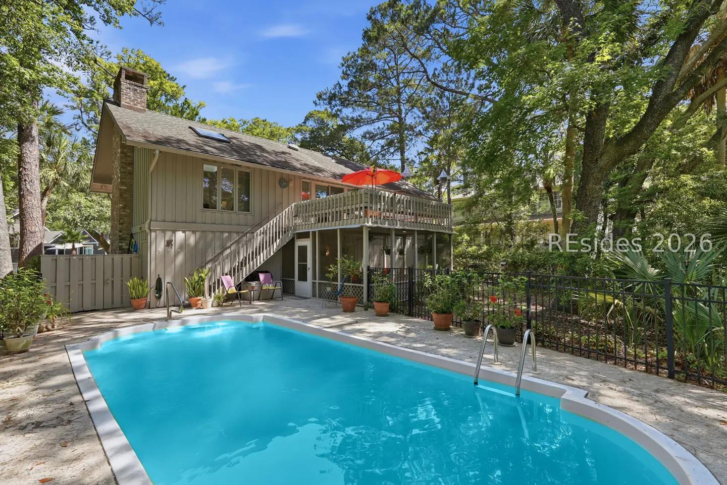 Backyard view of a two-story house with a pool. The house has a deck with an orange umbrella and stairs leading down to the pool area.
