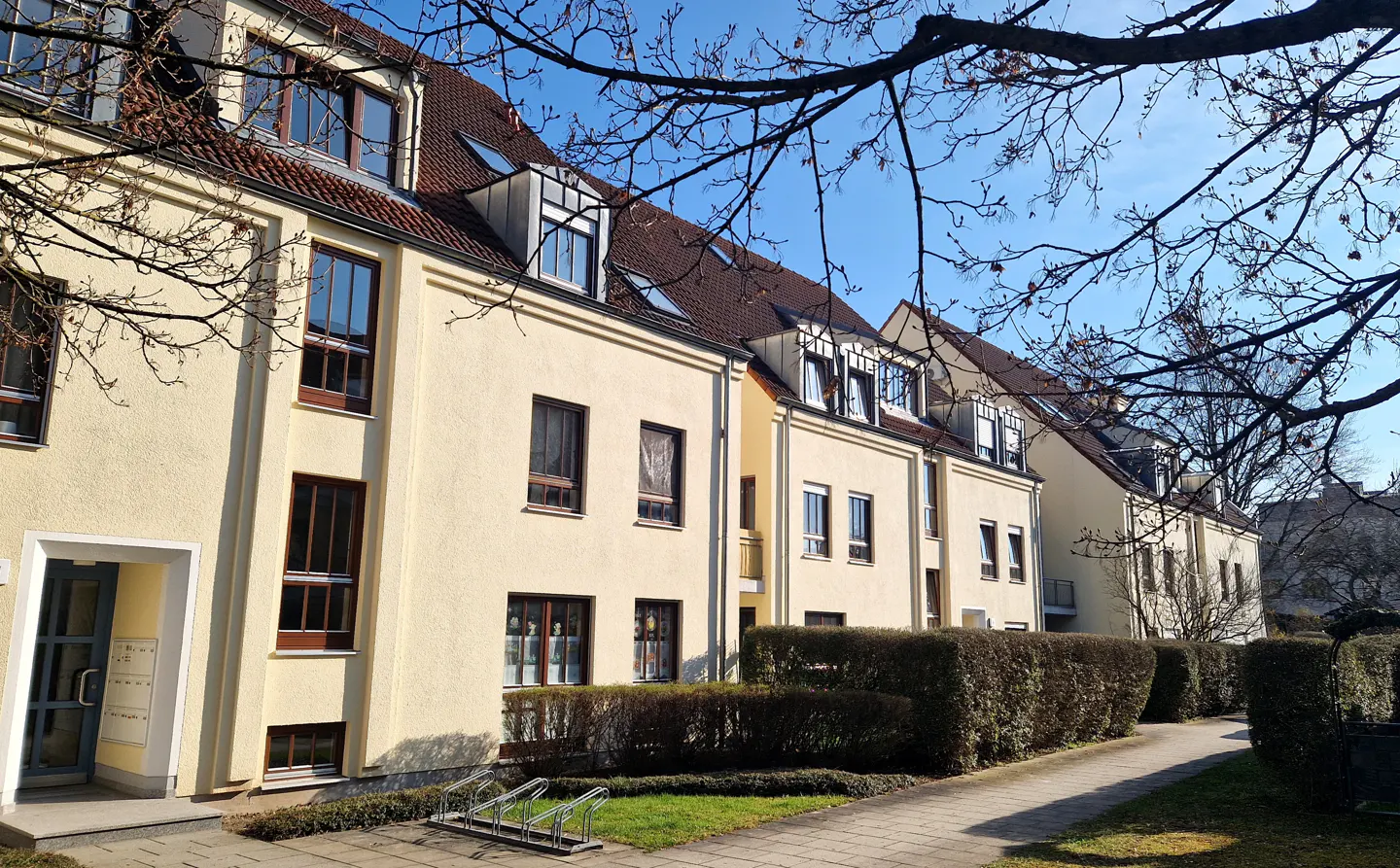 Row of cream-colored townhouses with brown roofs and windows under a blue sky.