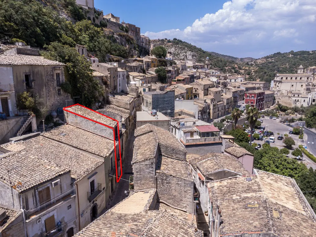 Aerial view of a building with a red outline in an Italian town. The building has a tiled roof and is surrounded by other buildings.