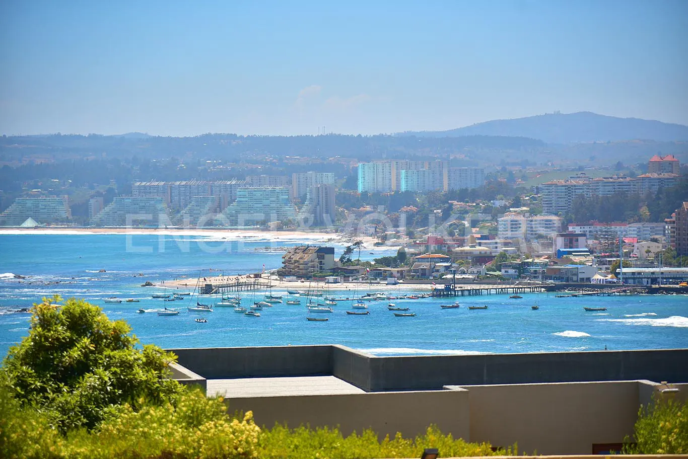 Ocean view of a coastal city with boats in the water, buildings, and mountains in the background.