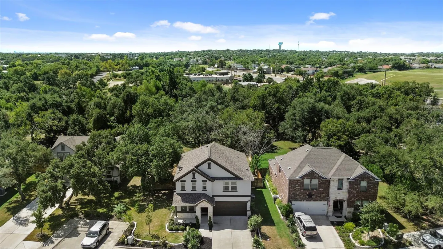 Aerial view of two-story homes with green trees, blue sky, and cars parked in driveways.