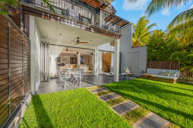 Modern home exterior with a patio, lawn, and outdoor seating. The interior is visible through open sliding glass doors.