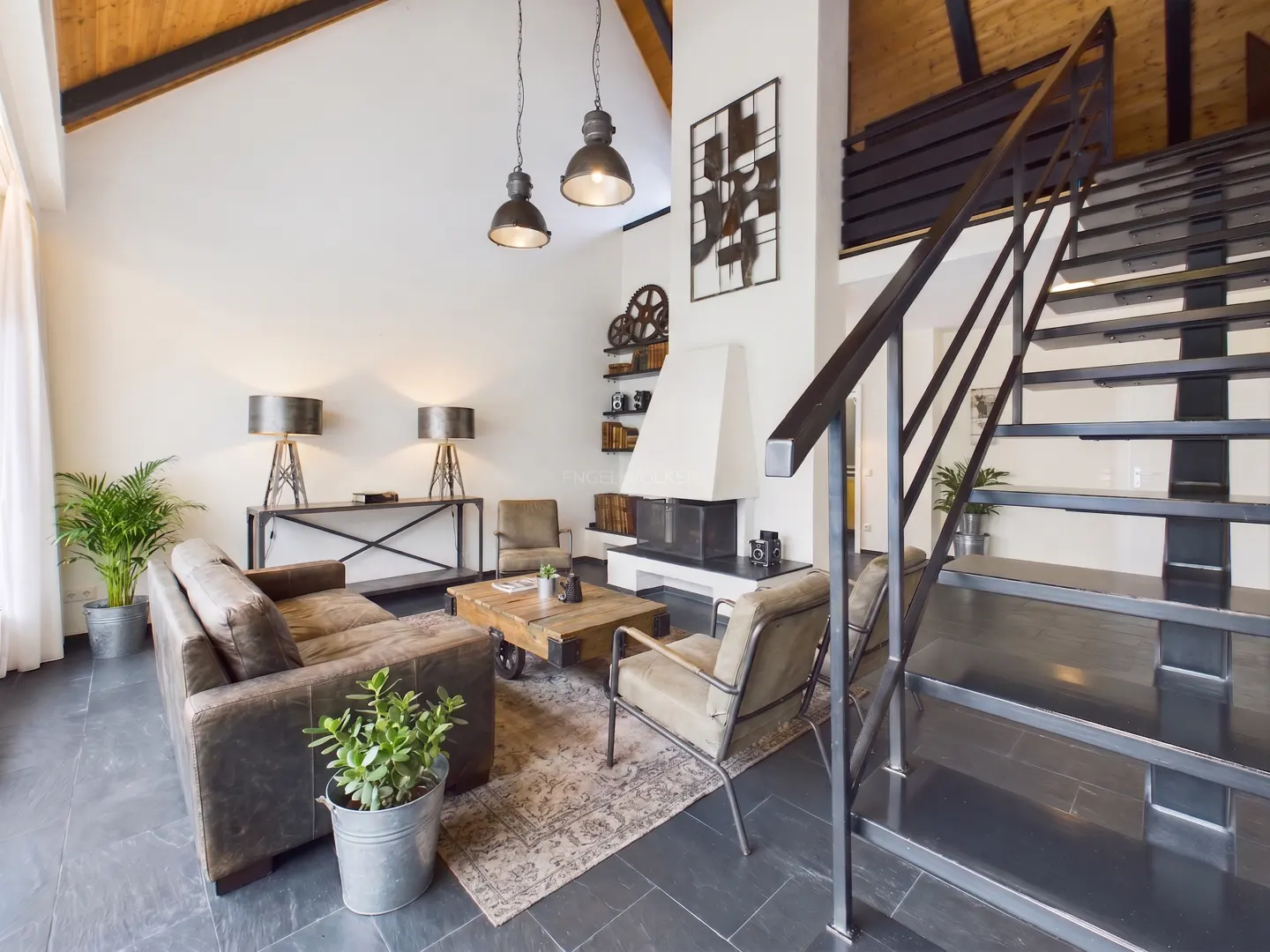 Industrial-style living room with leather sofa, metal staircase, fireplace, and vaulted wood-paneled ceiling.