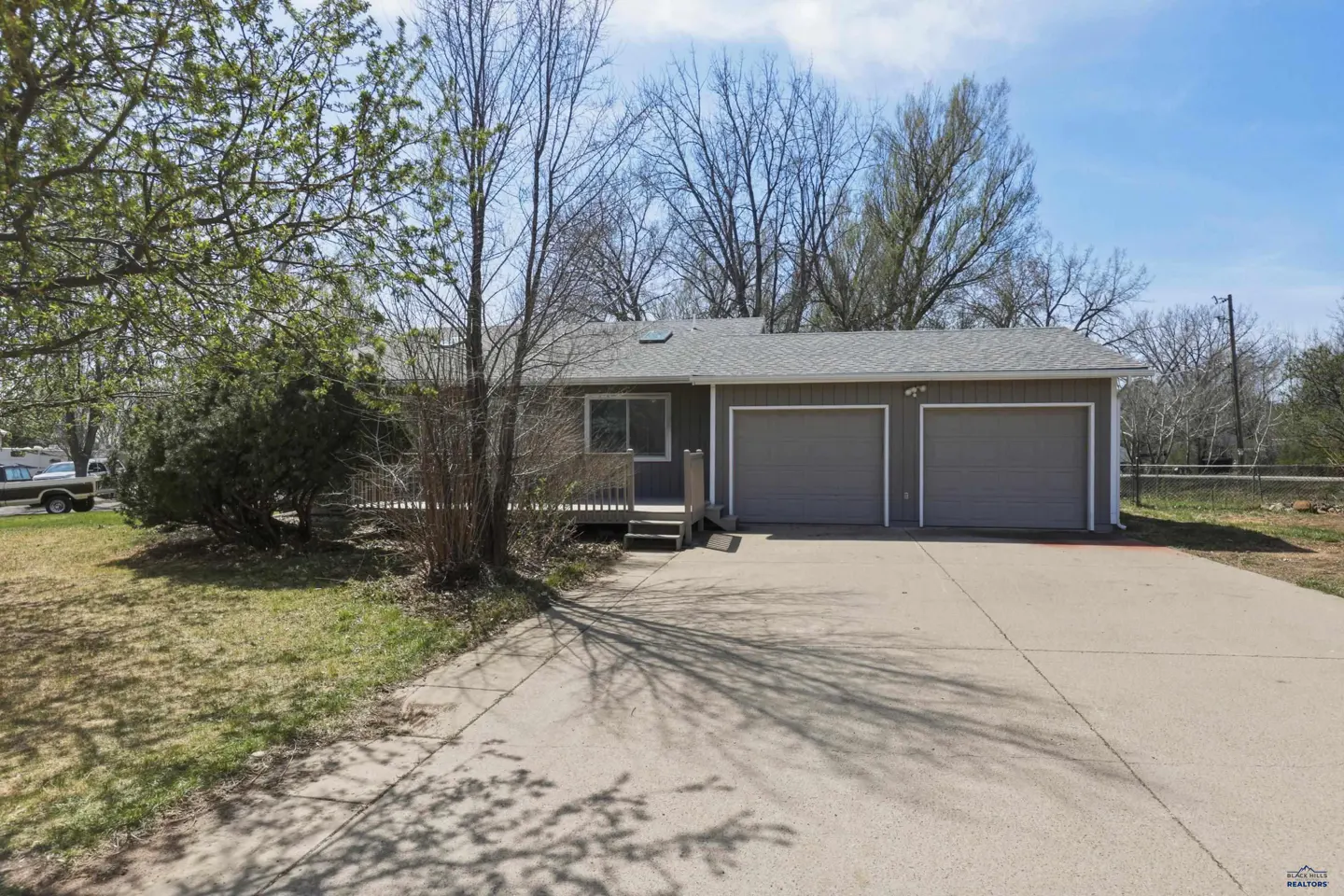 A gray single-story house with a two-car garage and a concrete driveway on a sunny day.