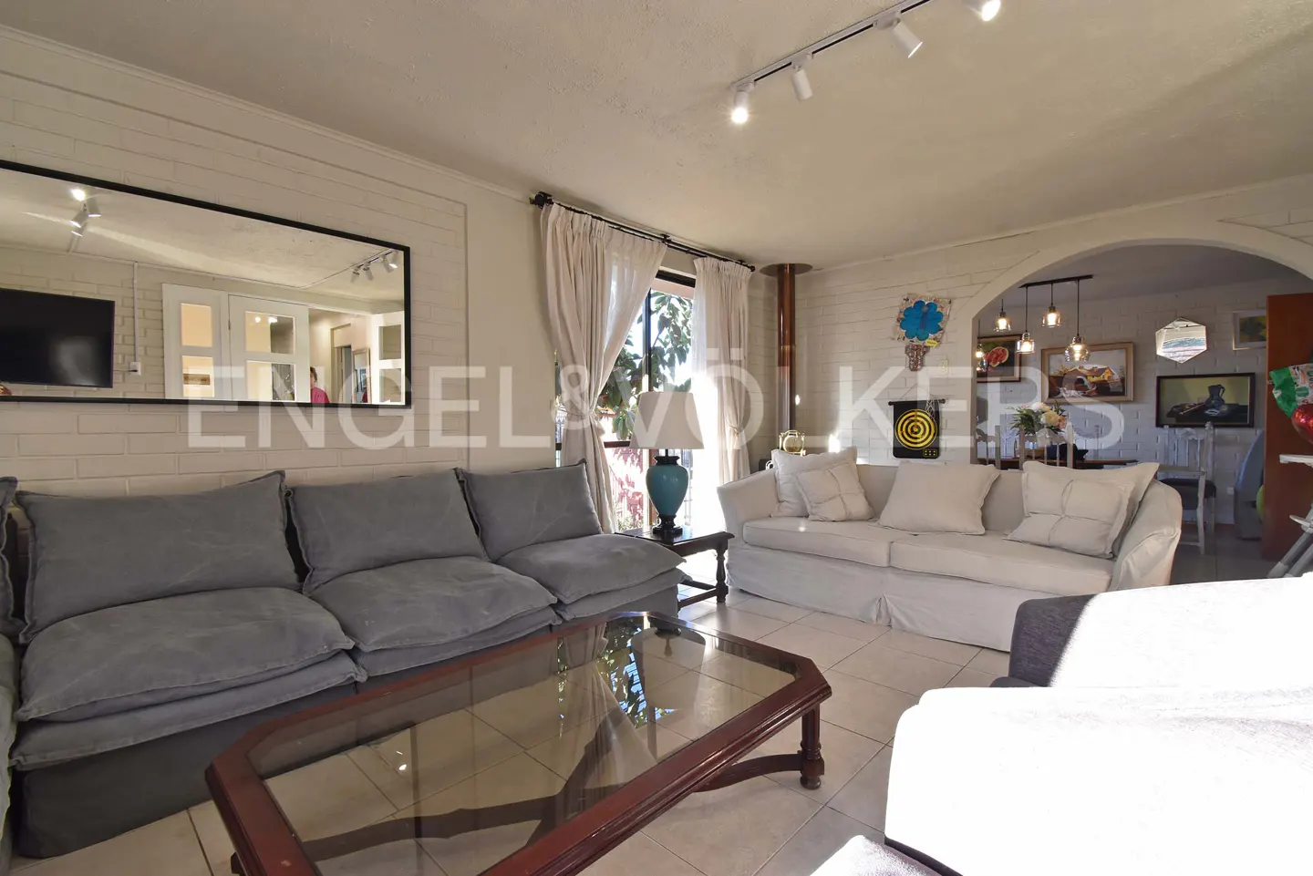 Living room with gray sofa, glass coffee table, and white sofa. A mirror hangs above the gray sofa.