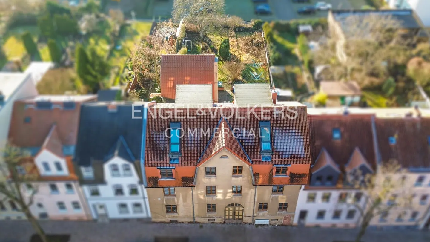 Aerial view of a commercial building with a red tile roof, surrounded by other buildings and greenery. "Engel & Volkers Commercial" overlayed.