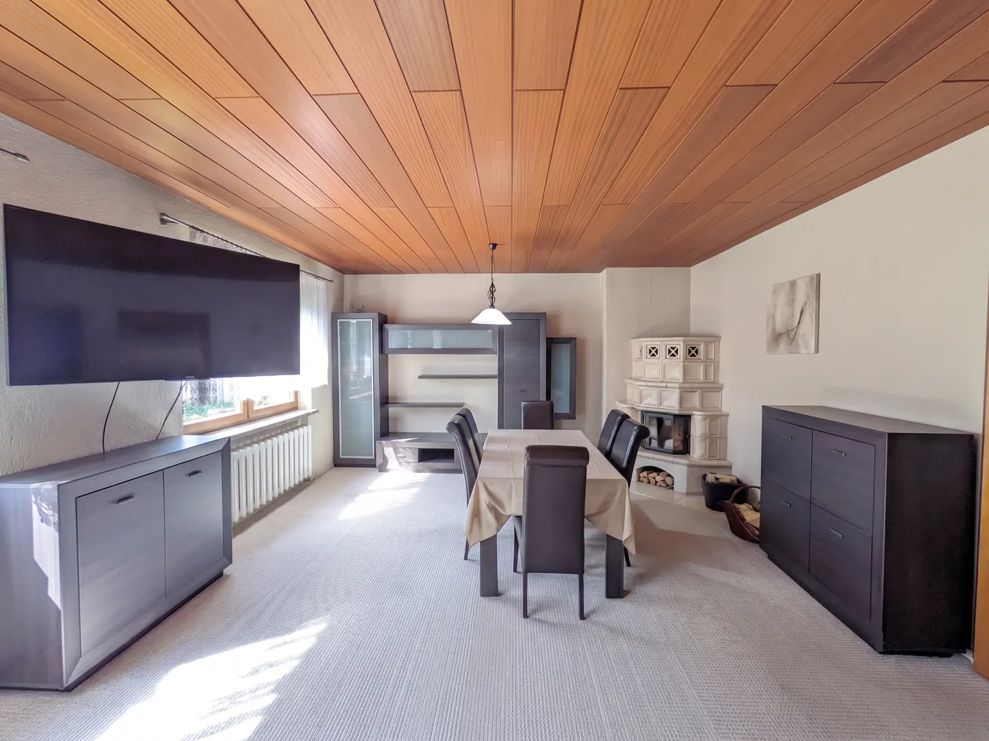 Dining room with wood-paneled ceiling, beige carpet, dark furniture, a dining table with chairs, and a tiled fireplace.