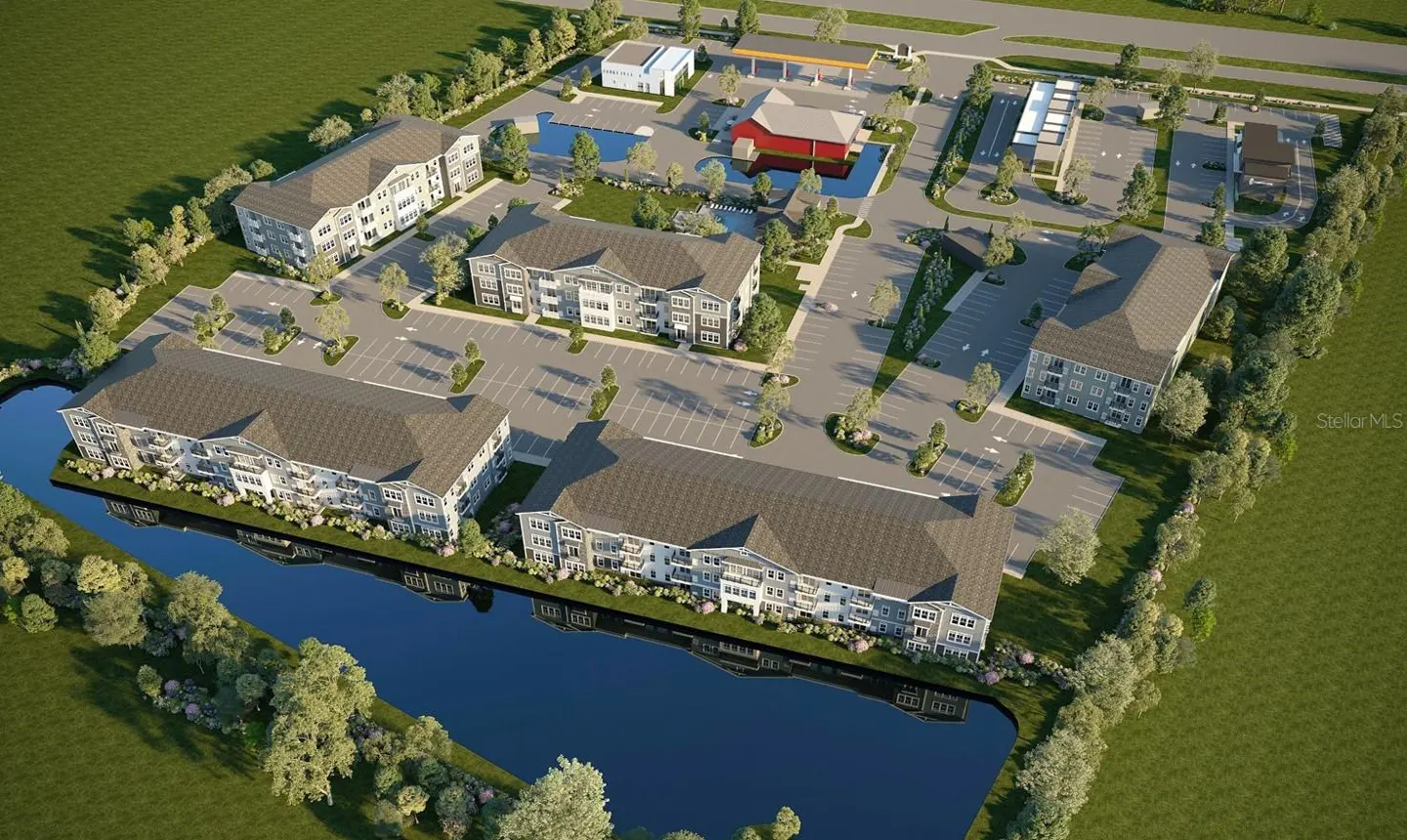 Aerial view of a gray apartment complex with parking, a pond, and commercial buildings.