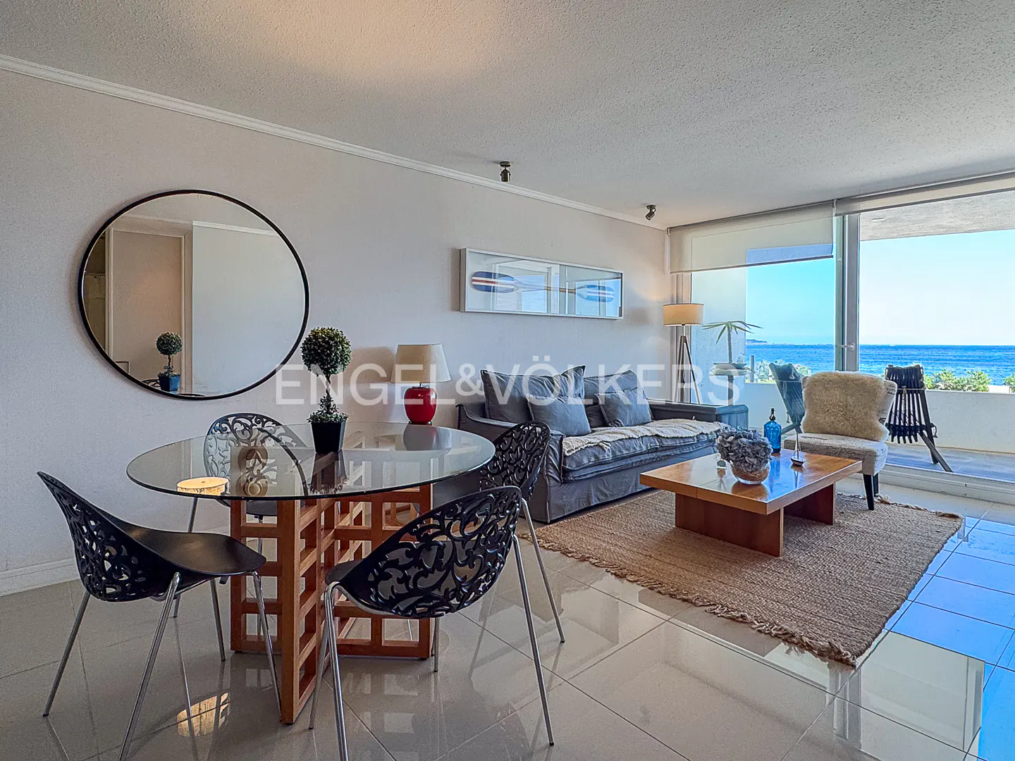 Bright living room with ocean view features a glass table with black chairs and a gray sofa on a jute rug.