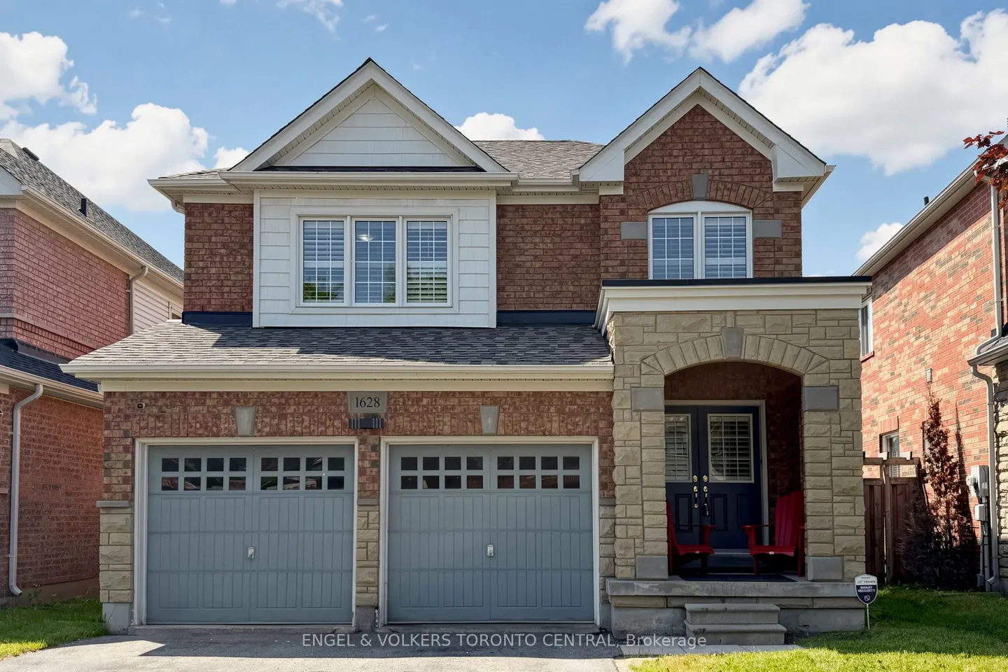 Two-story brick home with a stone-accented porch, two grey garage doors, and a blue front door under a blue sky.