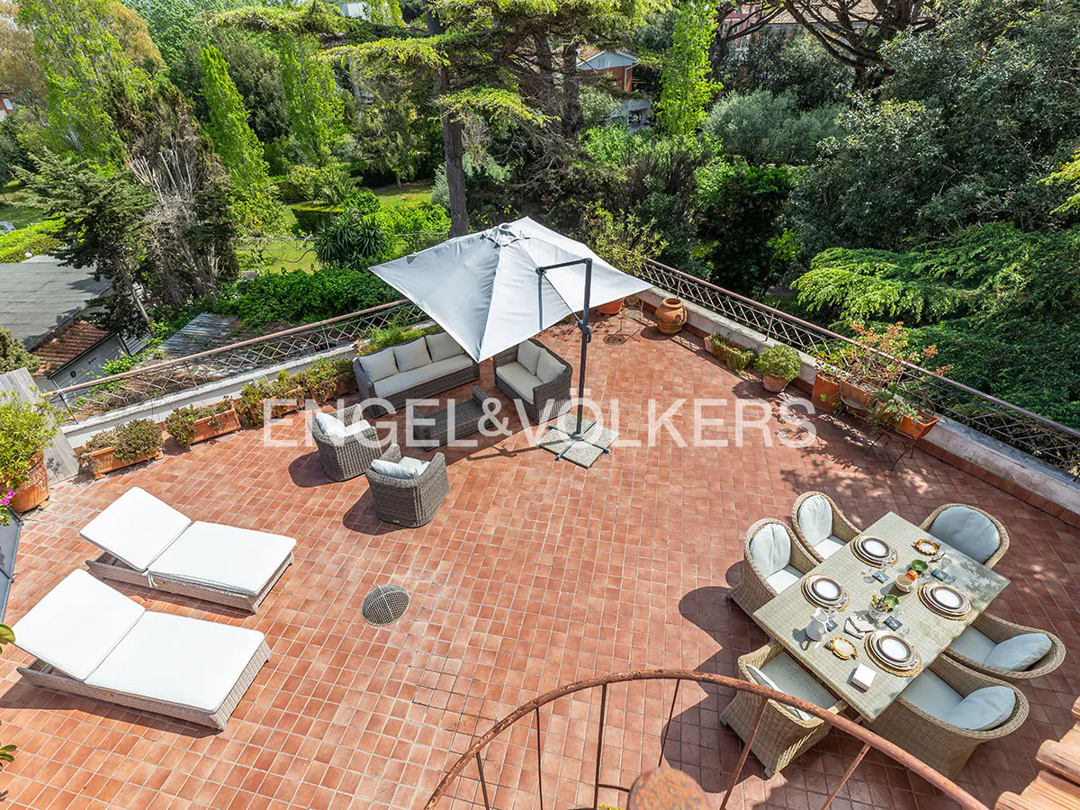 Aerial view of a red-tiled patio with outdoor furniture, including a dining table, lounge chairs, and sofas, surrounded by lush greenery.