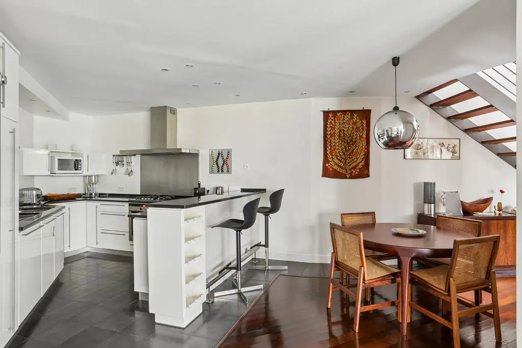 Modern kitchen with white cabinets, black counters, breakfast bar with stools, and a dining area with a round wood table.