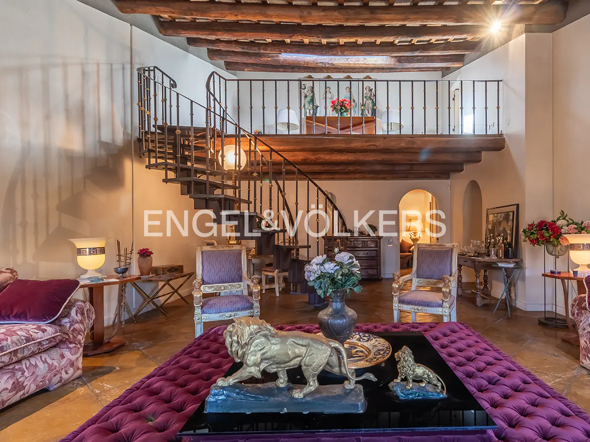 Interior view of a living room with a spiral staircase, wooden beams, and a purple tufted ottoman with lion statues.