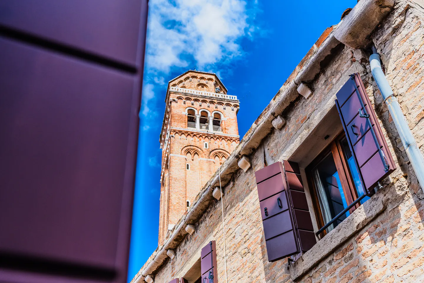 Low-angle shot of a brick building with brown shutters and a tall brick tower against a blue sky.
