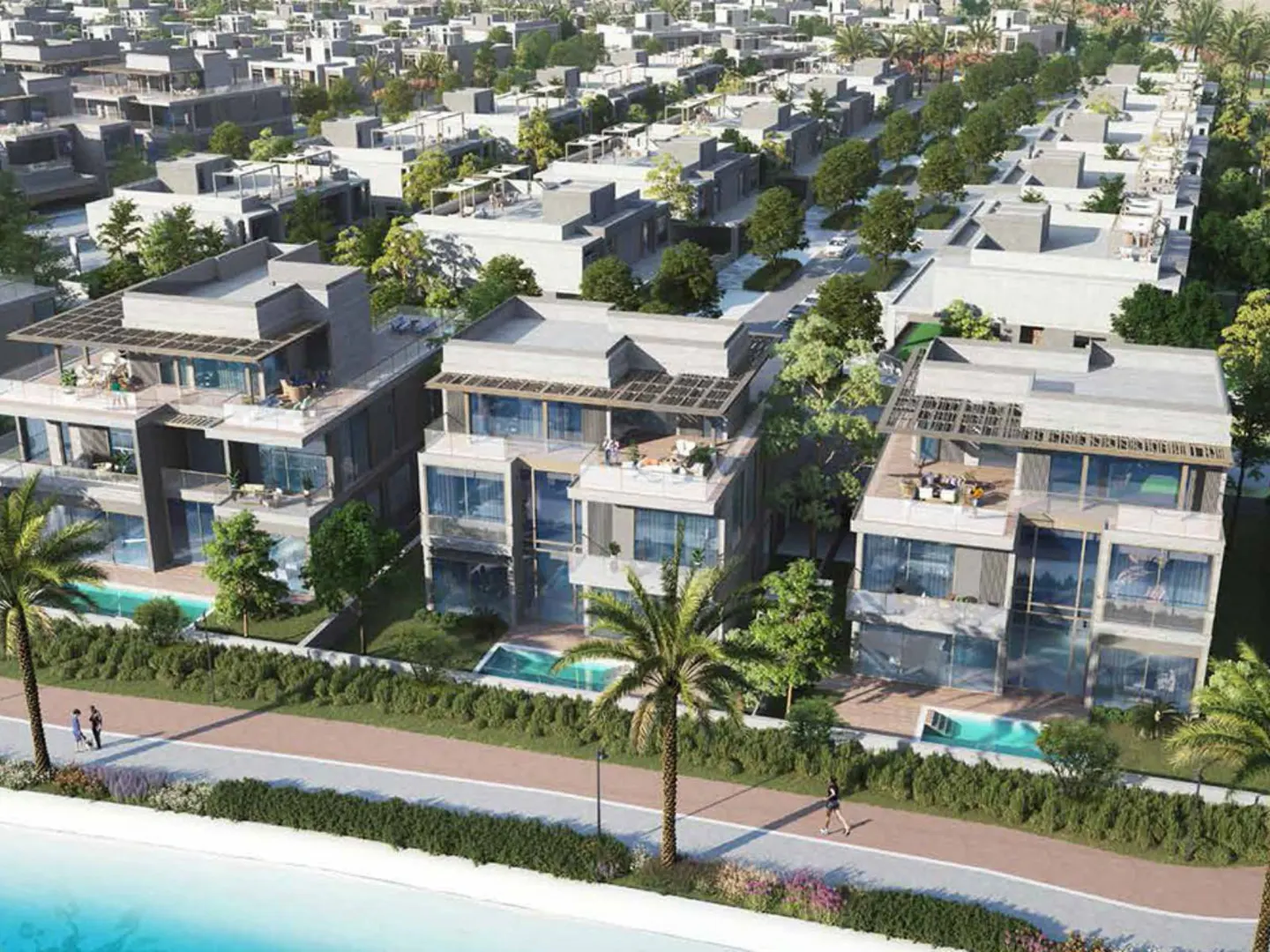 Aerial view of modern, multi-story gray houses with pools, palm trees, and green landscaping in a residential area near a beach.