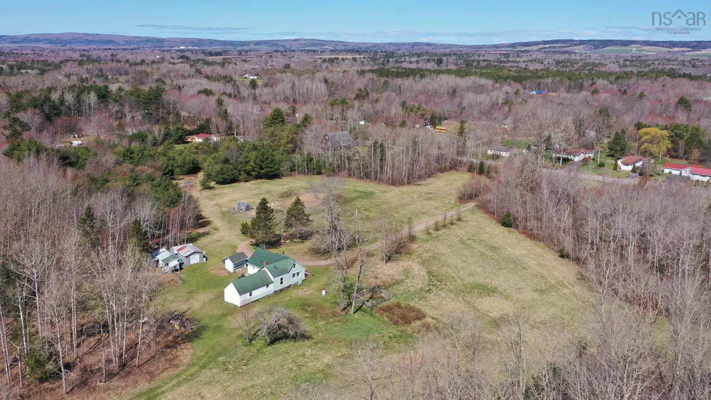Aerial view of a white house with a green roof, surrounded by fields and trees in a rural area.