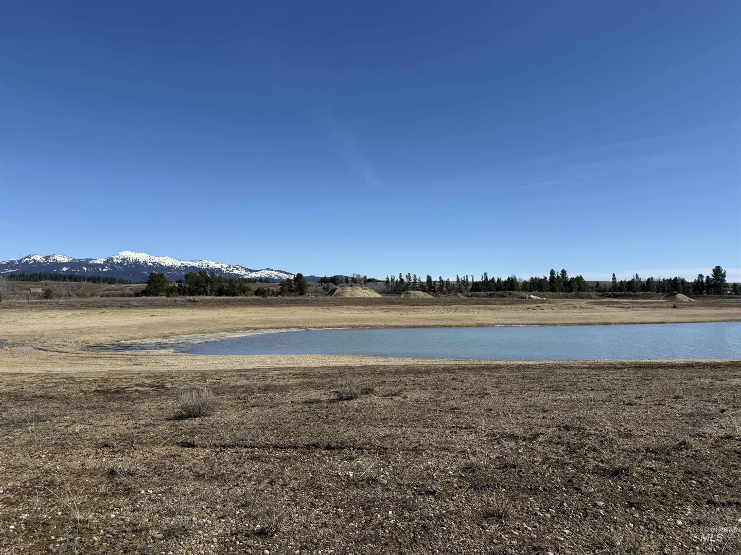 A landscape view of a pond with mountains in the background under a clear blue sky.