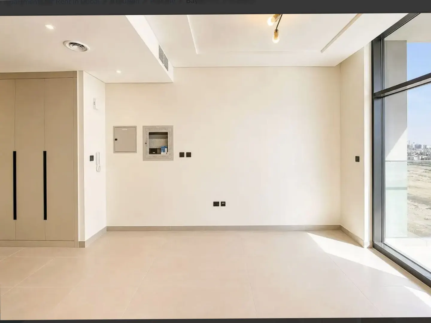 Empty room with beige walls, tile floor, and a large window showing a city view. A closet is on the left wall.